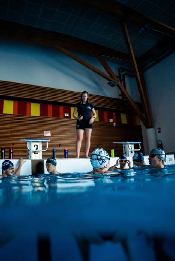 Des nageurs dans un bassin avec leur entraineur donnant des conseils